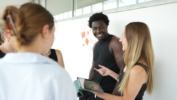 eine Studentin spricht mit 4 weiteren Studierenden. Sie hält ein iPad in ihrer Hand.