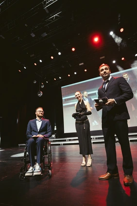 Student Lukas Gloßner mit zwei Moderierenden auf der Bühne bei der Akademischen Feier