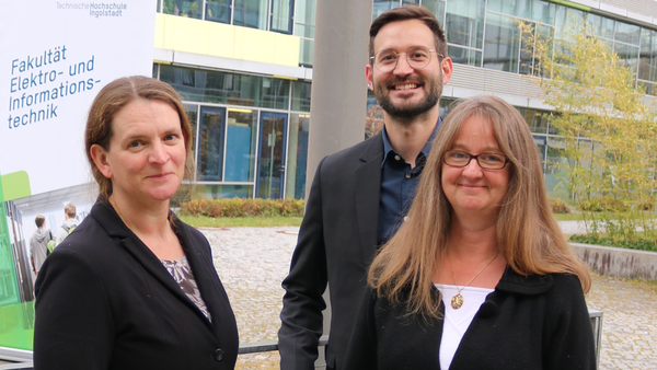 Three professors in front of the roll-up on the university campus