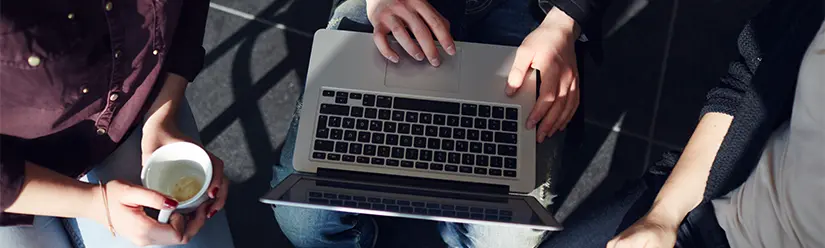 Blick von oben auf ein Laptop, darum 3 Personen